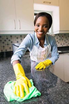 a woman in an apron and yellow gloves cleaning a kitchen counter