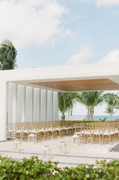 an outdoor wedding venue set up with gold chairs and palm trees on the beach behind it