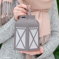 a woman holding a gray lantern in her hands with a scarf around her neck,