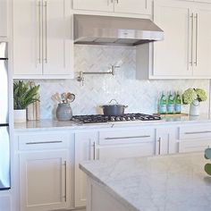 a kitchen with white cabinets and marble counter tops, stainless steel range hood over the stove