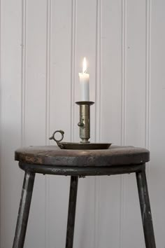 a lit candle sitting on top of a wooden table next to a metal tray with a handle