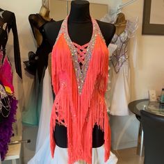 a mannequin wearing an orange fringed top in a clothing store with other dresses on display