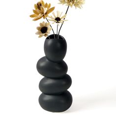 a black vase filled with flowers on top of a white table next to a stack of rocks