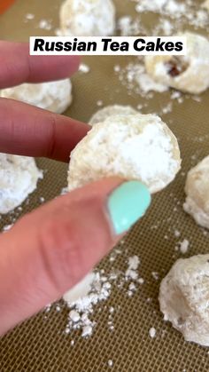 a hand is pointing at russian tea cakes on a baking sheet with powdered sugar