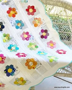 a white quilt on a wicker chair next to a basket filled with colorful flowers