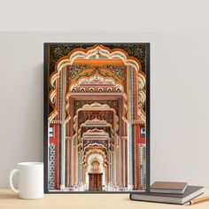 a coffee mug sitting on top of a wooden table next to a book and an art print