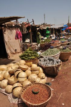 an open air market with lots of vegetables and fruits on the ground in front of it