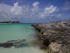 the water is crystal blue and clear with clouds in the sky above it, as well as some rocks on the shore