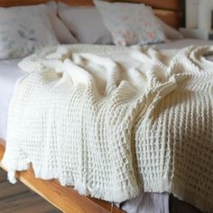 a white blanket on top of a wooden bed with pillows and blankets over the headboard