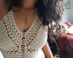 a woman wearing a white crochet top with tattoos on her chest and arm