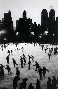 many people are skating on an ice rink at night with lights shining in the background