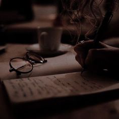 a person writing on top of a piece of paper next to a cup of coffee