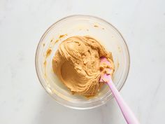 a bowl filled with peanut butter next to a pink toothbrush on top of a white counter