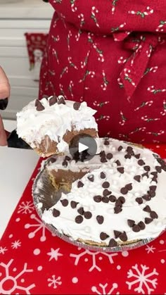 someone cutting into a cake on top of a red tablecloth with white snowflakes