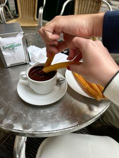 a person dipping something into a cup of coffee on top of a saucer and plate