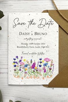 save the date card with wildflowers on it next to a brown envelope and green leaves