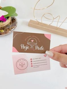 a person holding up a business card next to a bowl of flowers on a table