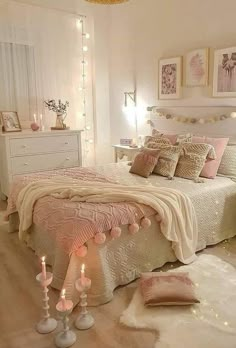 a bedroom decorated in pink and white with candles on the bed, lights strung from above