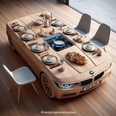 a table made out of a bmw car with plates and bowls on it, surrounded by chairs