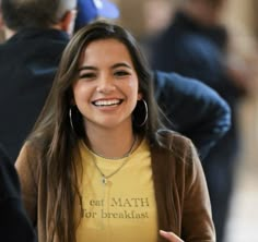 a smiling young woman in a yellow shirt and brown cardigan is talking to someone