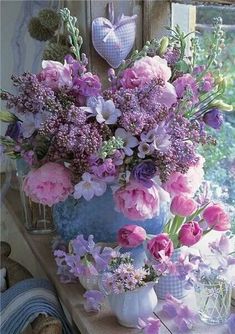 a vase filled with lots of purple flowers on top of a table next to a window