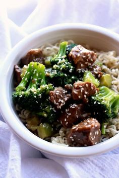 a white bowl filled with meat and broccoli on top of rice covered in sesame seeds