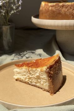 a piece of cheesecake sitting on top of a plate next to a vase with flowers