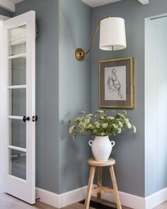 a white vase with flowers sitting on top of a wooden stool next to a doorway