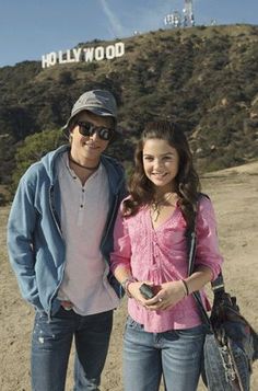 a man standing next to a woman in front of a hollywood sign on top of a hill