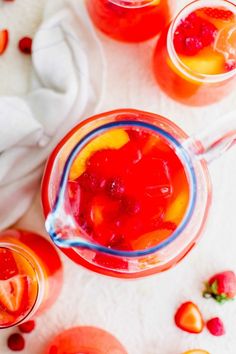 two glasses filled with liquid and fruit on top of a white surface next to oranges