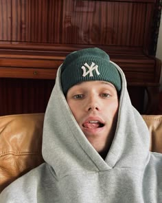 a young man wearing a new york yankees hoodie making a surprised face while sitting on a couch