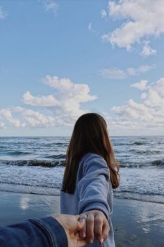 two people holding hands on the beach with waves in the water and clouds in the sky