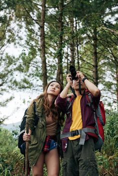 two people standing in the woods taking pictures