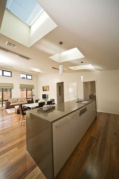 an open kitchen and living room with wood flooring in the middle, along with skylights