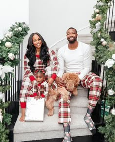 a man and woman are sitting on the steps with their two children wearing matching plaid pajamas