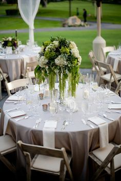 the table is set with white linens, silverware and green floral centerpieces