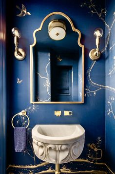 a bathroom with blue walls and gold trimmings on the mirror, sink and toilet