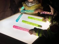 two children are playing with glow sticks on the table in front of them, and one child is looking at it