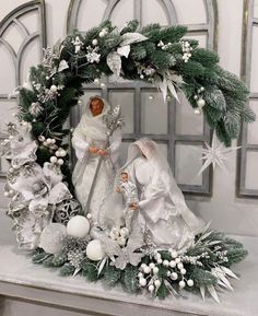 two figurines are sitting in front of a christmas wreath