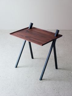 a wooden table sitting on top of a cement floor next to a white wall and black metal legs