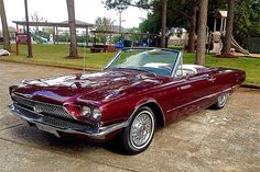 a red convertible car parked in front of a park