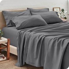 a bed covered in grey sheets and pillows