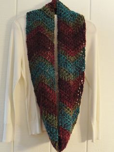 a knitted scarf hanging on a wall next to a white t - shirt and wooden hanger