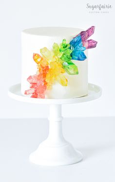 a multicolored cake on a white pedestal with the frosting and icing flowers