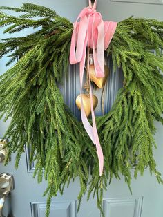 a wreath with bells and pink ribbon hanging on the front door to welcome someone or someone