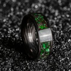 a wedding band with green and white glitter inlays on black wood grain background