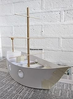 a model boat sitting on top of a table next to a wall with newspaper pages