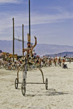 a man riding on the back of a tricycle across a sandy beach covered in people