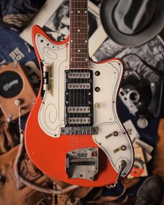 an old red guitar sitting on top of a pile of other musical instruments and memorabilia