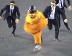 three men in suits and hats are running down the street with one man dressed as a sesame character